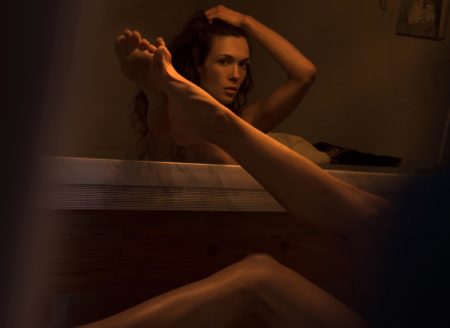 Naked model lying infant of mirror with one leg on the mirror